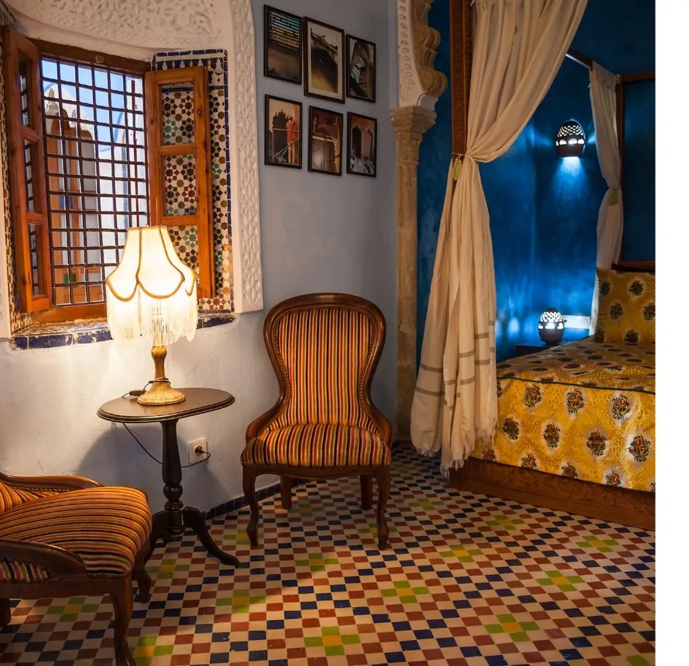 Une chambre, lit au couvre-lit jaune, fauteuils et fenêtre en bois