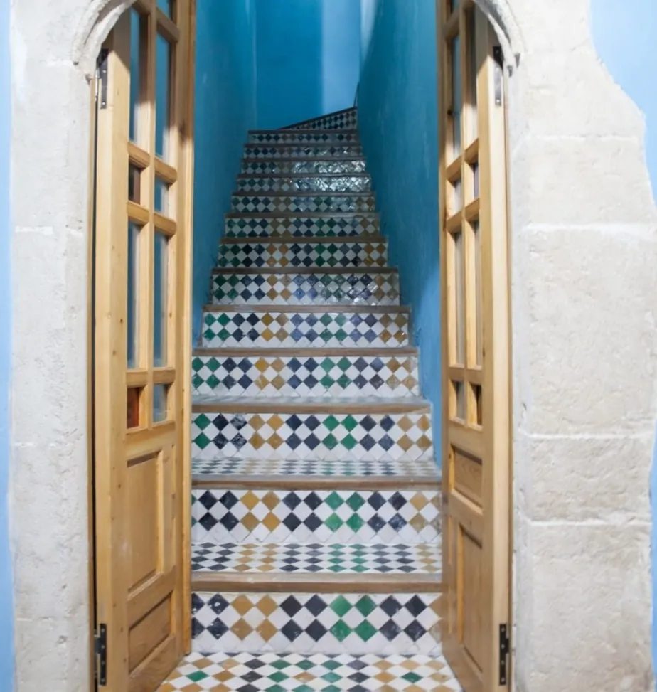 L’escalier de zellige entre deux portes en bois, murs bleus