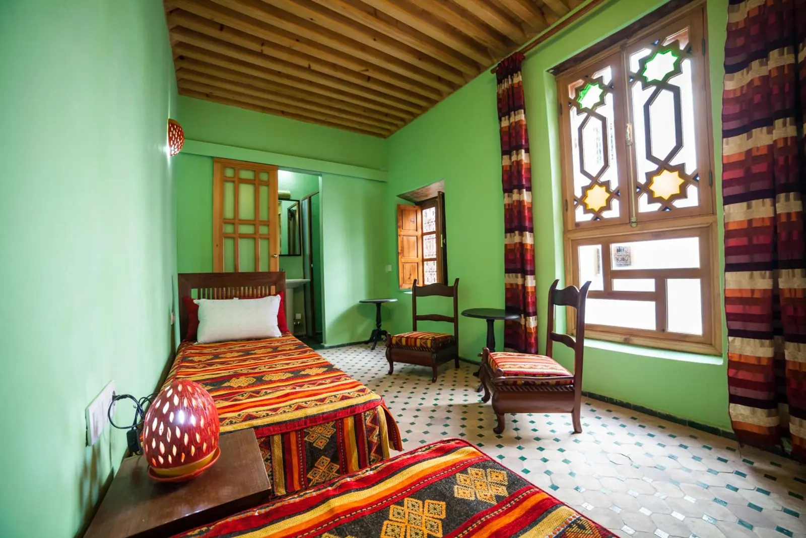 La chambre lits jumeaux, murs verts et fenêtre en bois sculpté
