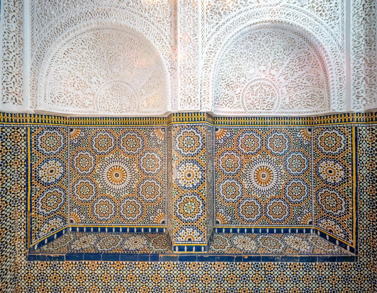 Un mur de zellige sous des arcs de plâtre sculpté